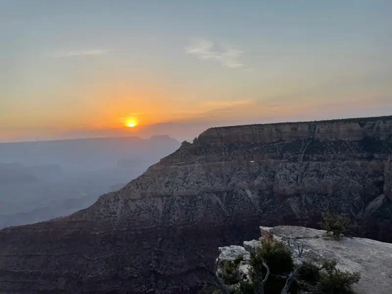 The sun rising above a broad canyon landscape.