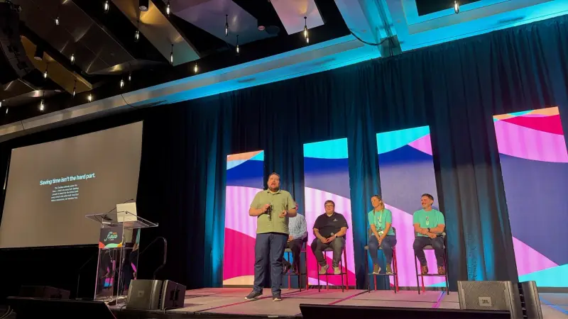A presenter and seated panel on the FLOW conference stage.