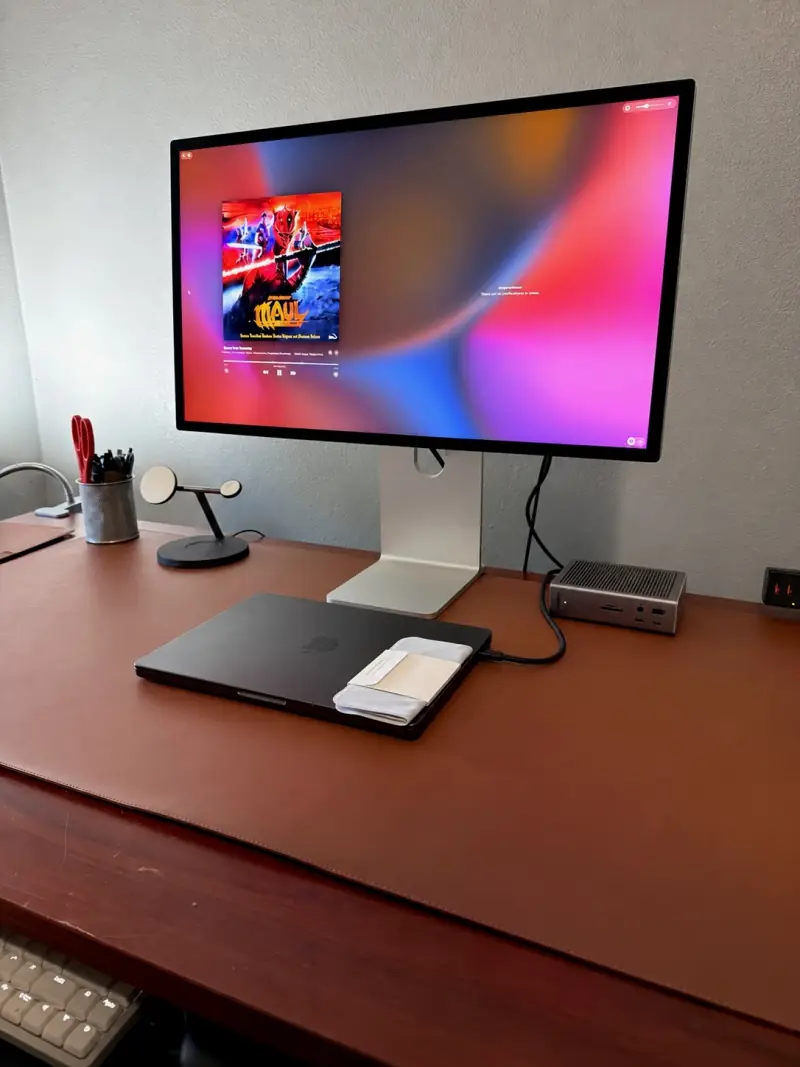 A Studio Display on a wooden desk with a laptop and peripherals.